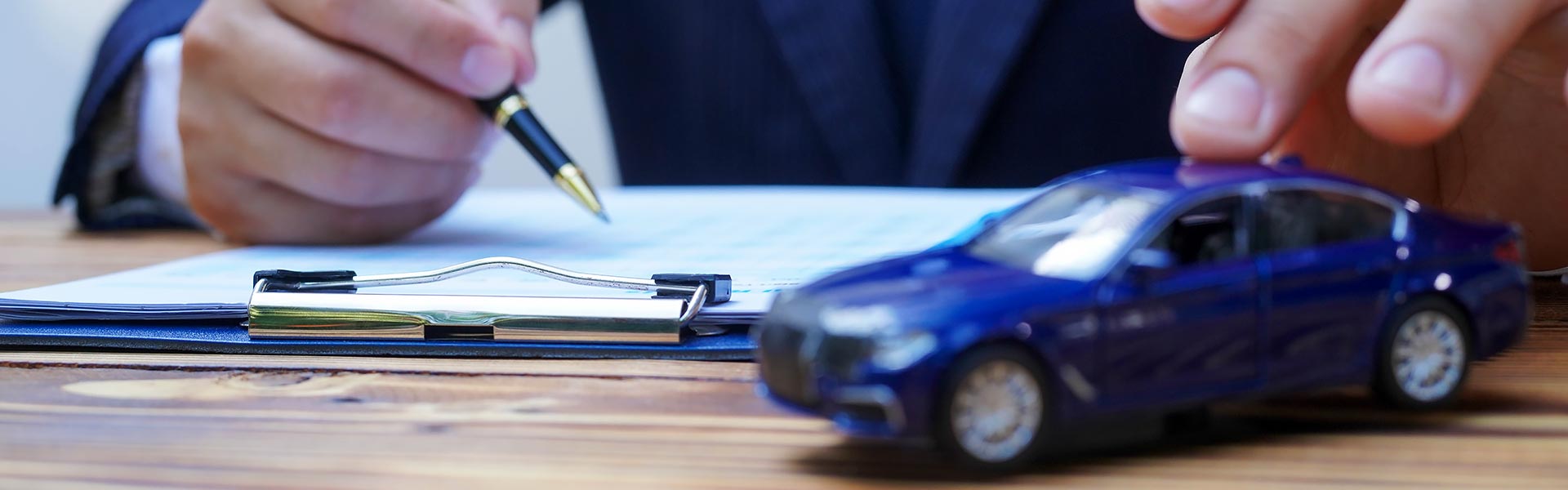 A person in a suit holding a pen while writing on a clipboard with a toy car nearby.