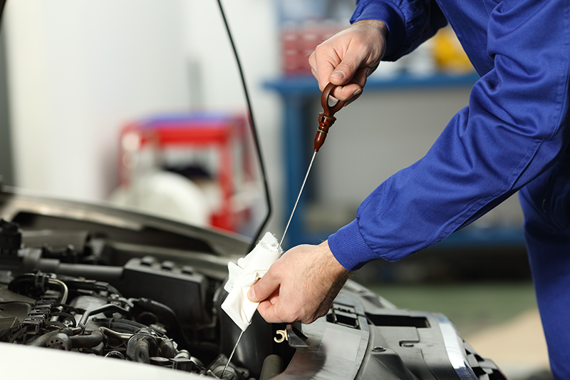 A mechanic in blue overalls checks the oil level of a car's engine using a dipstick.