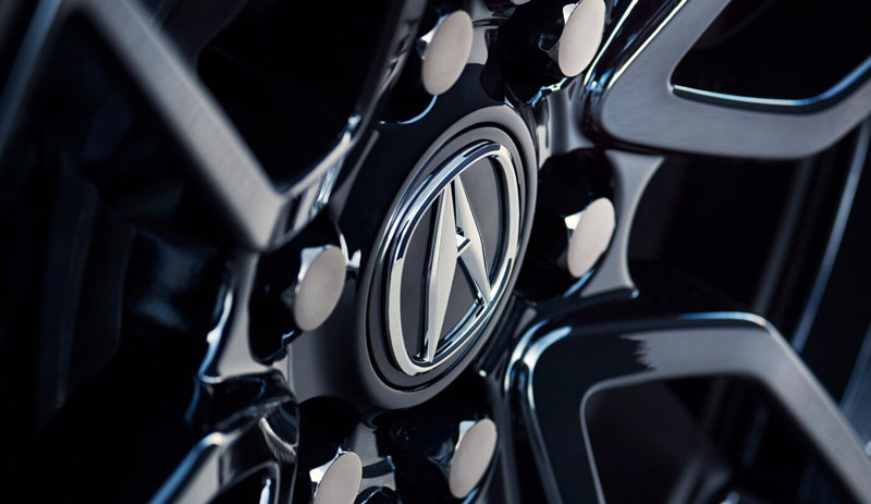 Close-up of a shiny black Acura wheel with silver lug nuts and logo.