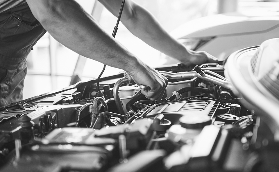 A mechanic working on a car engine, using tools and inspecting parts.